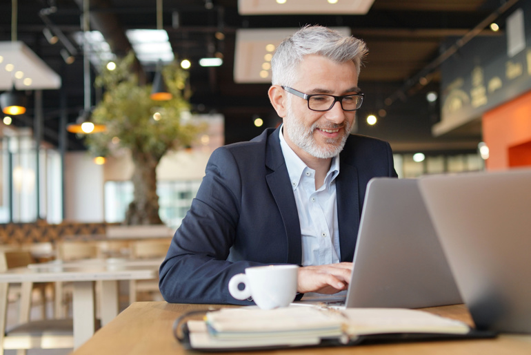 Grey-haired man on laptop in cafe