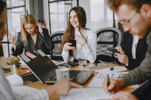 Professionals in a meeting room using phones and laptops during a workplace discussion.