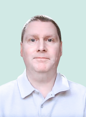 A man with short hair wearing a light gray collared shirt looks directly at the camera, with a neutral expression, against a plain light blue background.