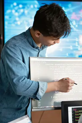 Software Developer stood at computer, pointing at lines of code on the screen.