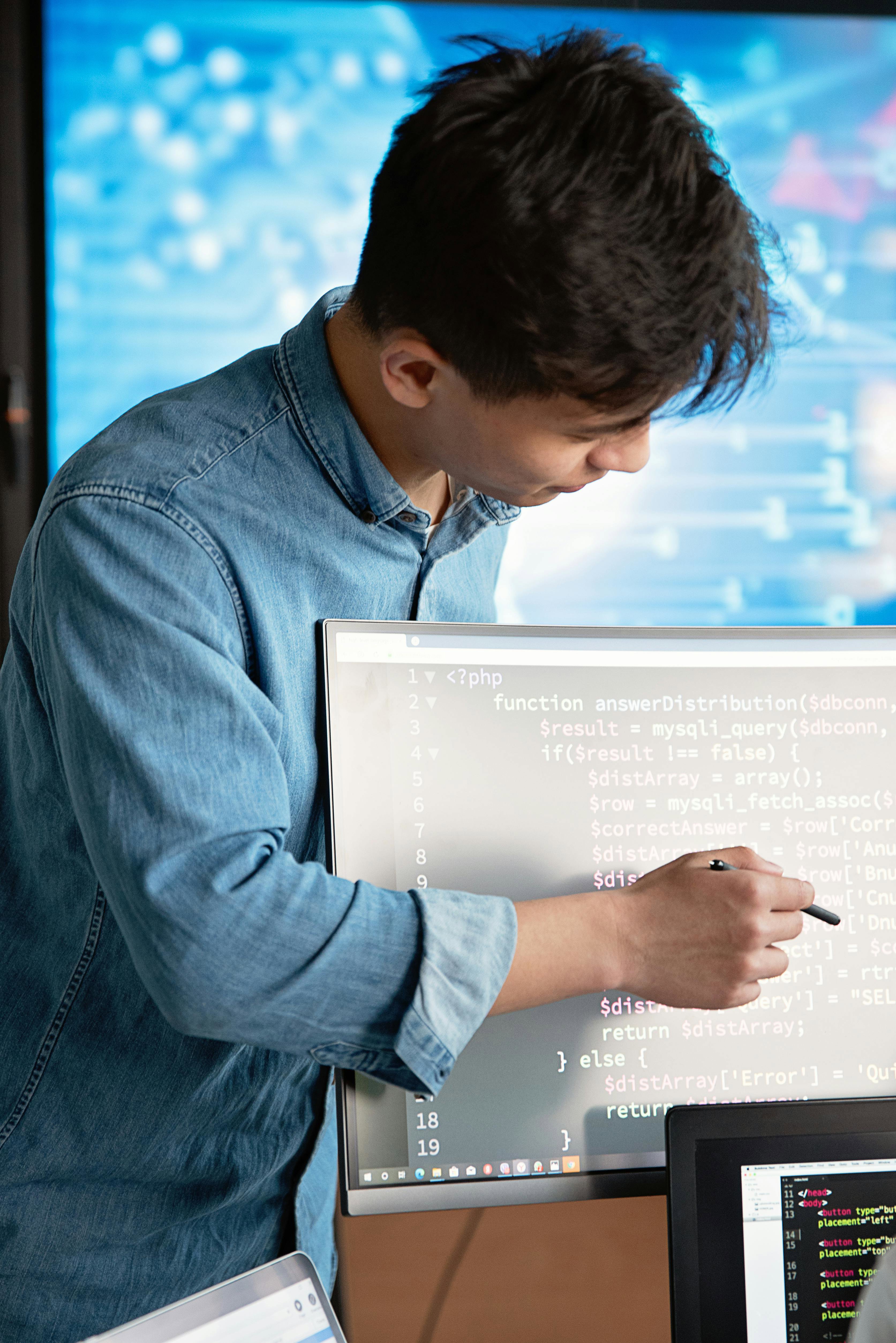 Software Developer stood at computer, pointing at lines of code on the screen.