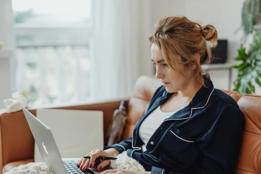 A young woman sits on a sofa using her laptop to search and apply for jobs after university, trying to secure her first graduate role.