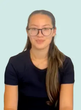 A young woman with long brown hair, glasses, and a black shirt sits against a light blue background, facing the camera and smiling slightly.