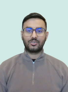 A person wearing glasses and a gray zip-up sweater is speaking while facing the camera against a light blue background.