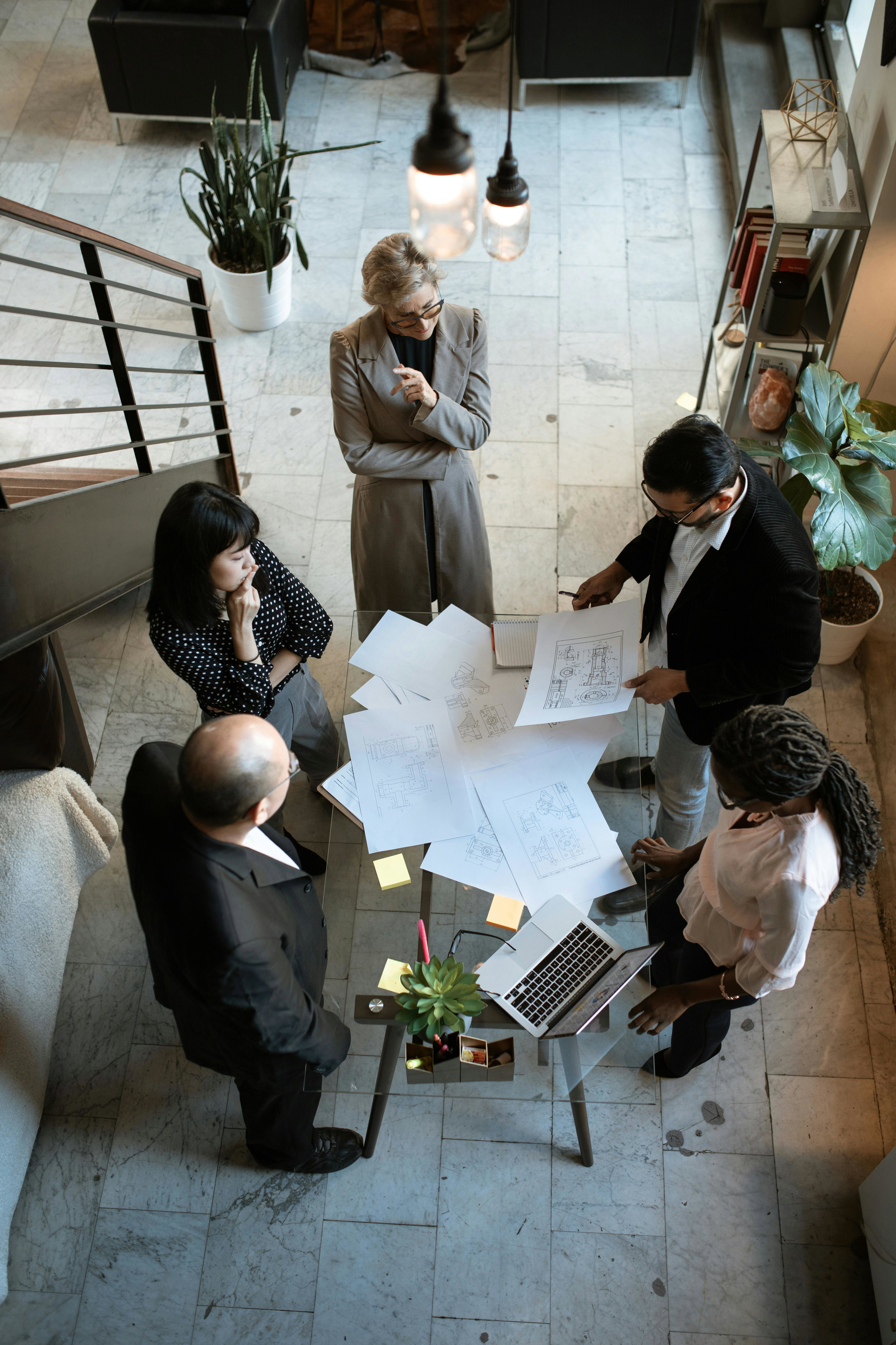 Overhead view of three people standing in an office, engaged in conversation. Two are facing each other, while the third stands with arms crossed. The image has a green color overlay and horizontal lines.