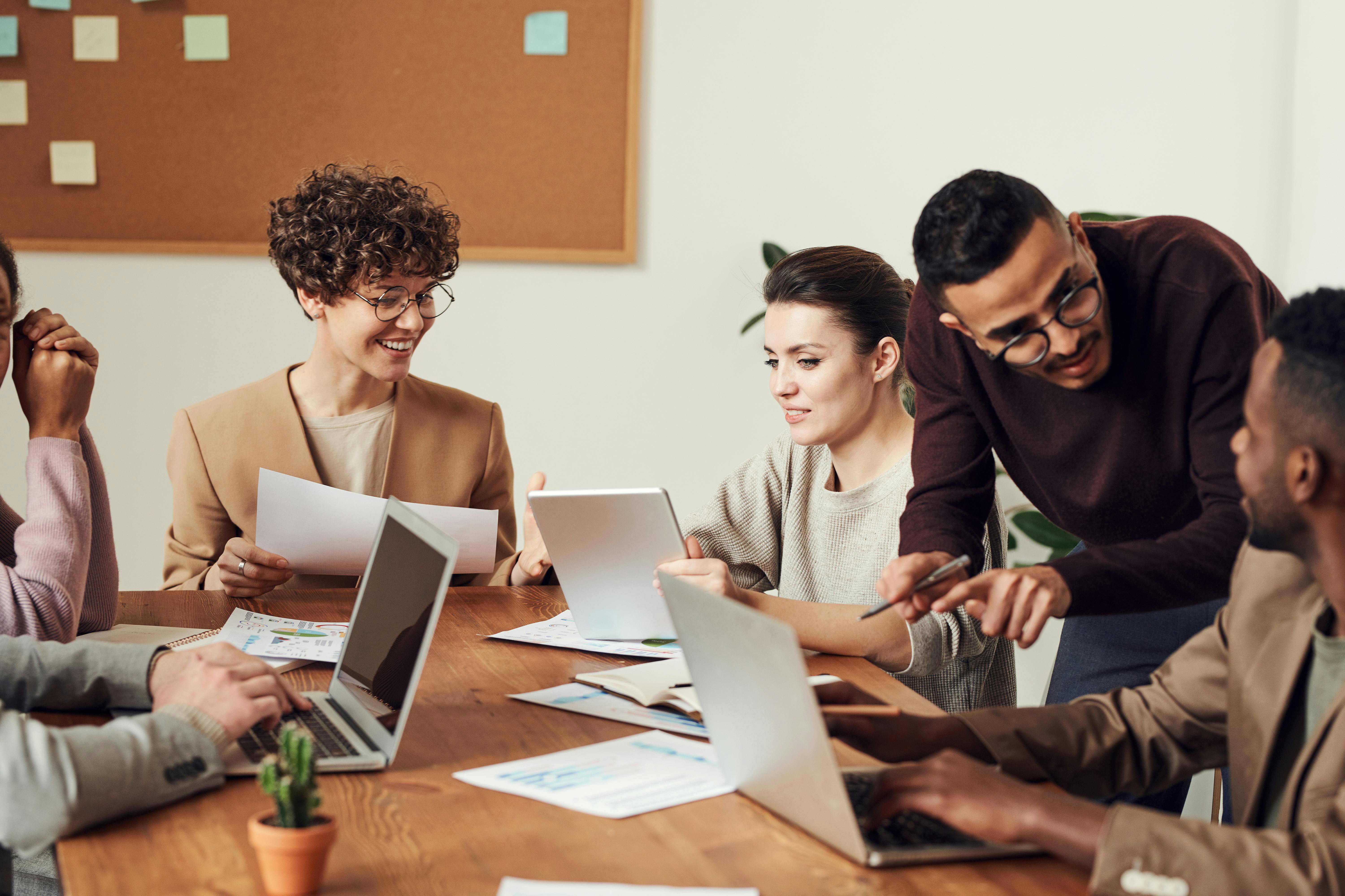 A Group Of Professionals Collaborating Around A Table Reviewing Documents And Working On Laptops During A Team Meeting