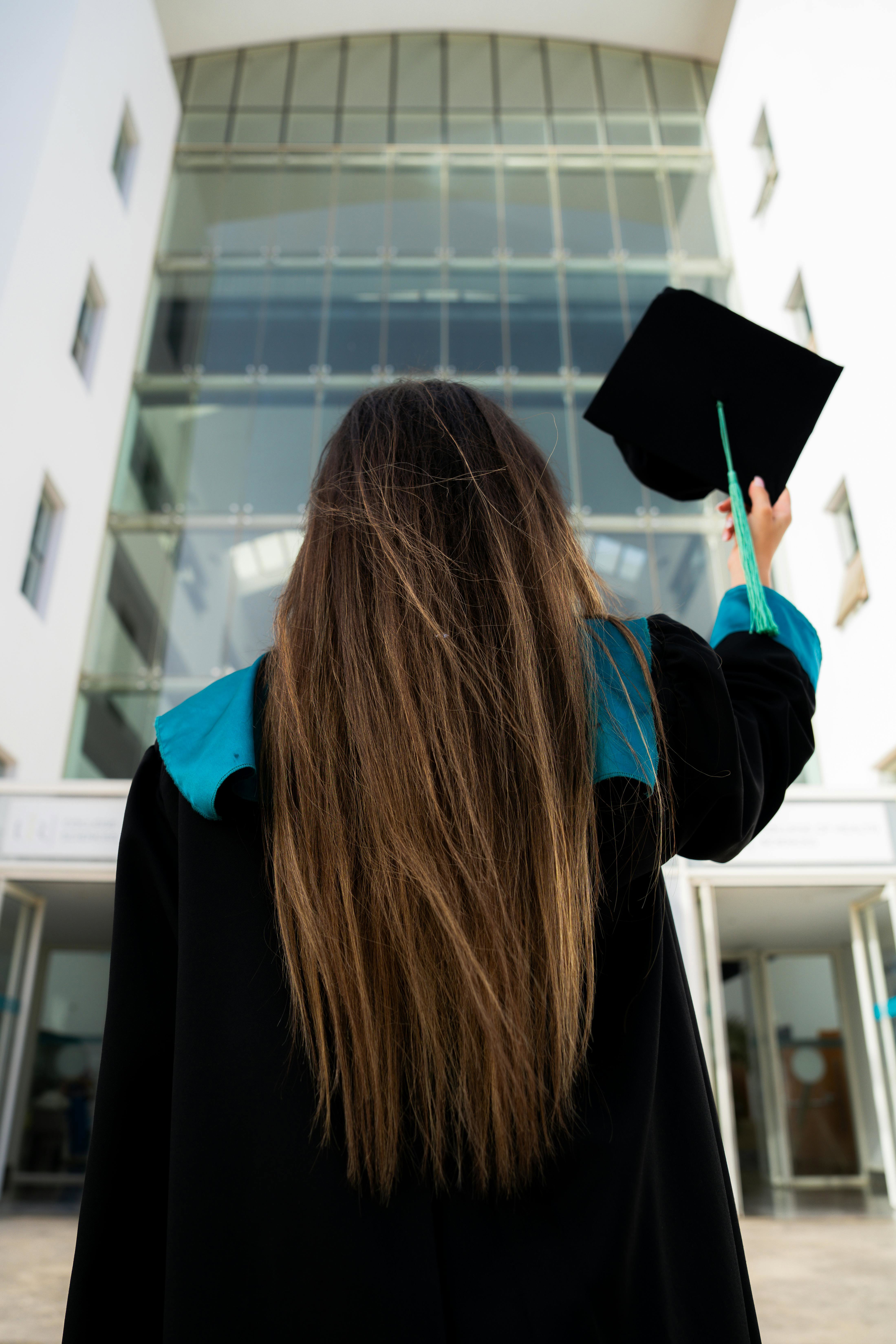 A university graduate dressed in robes and holding up their mortarboard. 
