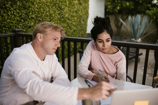 Two people reviewing notes and working together on a laptop during a focused study session outdoors.
