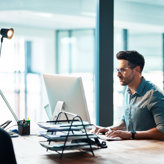 A professional man working on a laptop at a desk in an office environment.