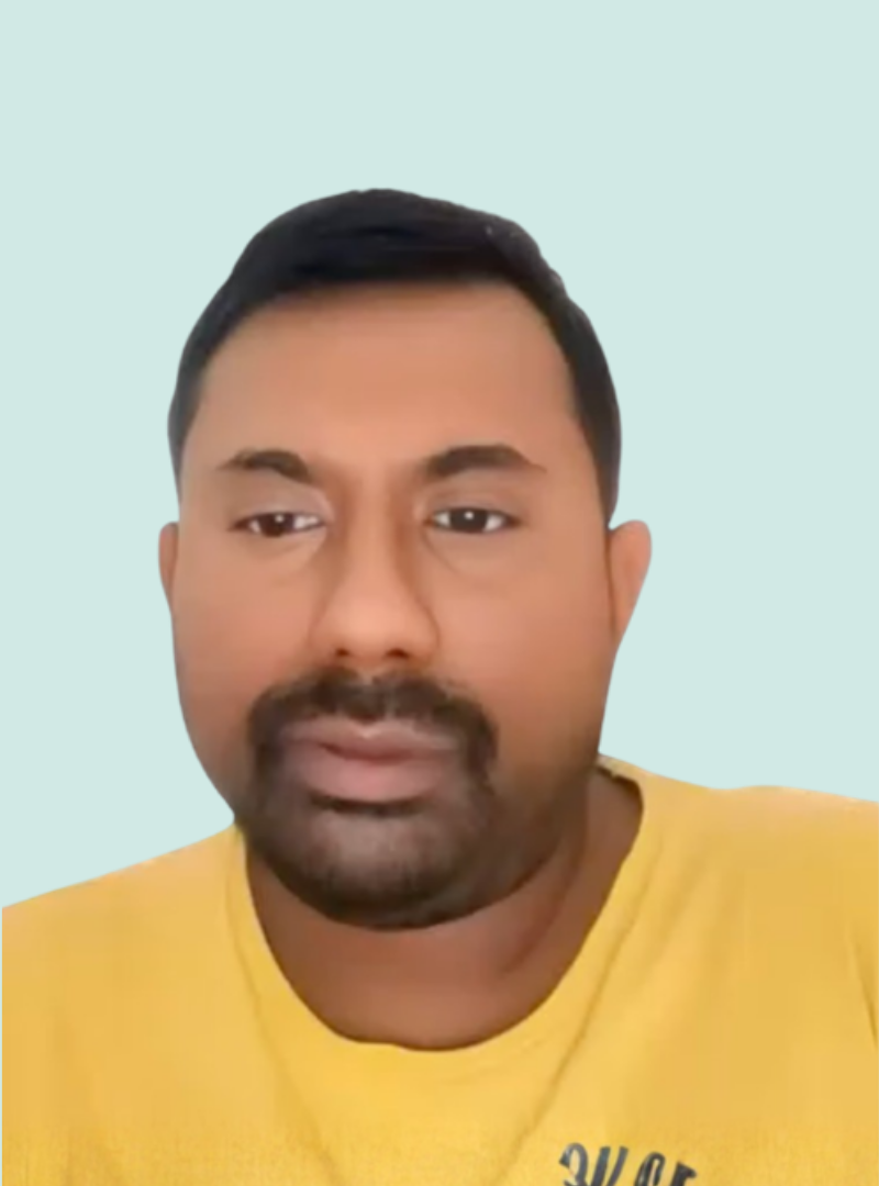 A man with short black hair and a beard wears a yellow shirt and looks ahead with a neutral expression against a plain light blue background.