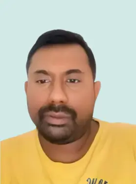 A man with short black hair and a beard wears a yellow shirt and looks ahead with a neutral expression against a plain light blue background.