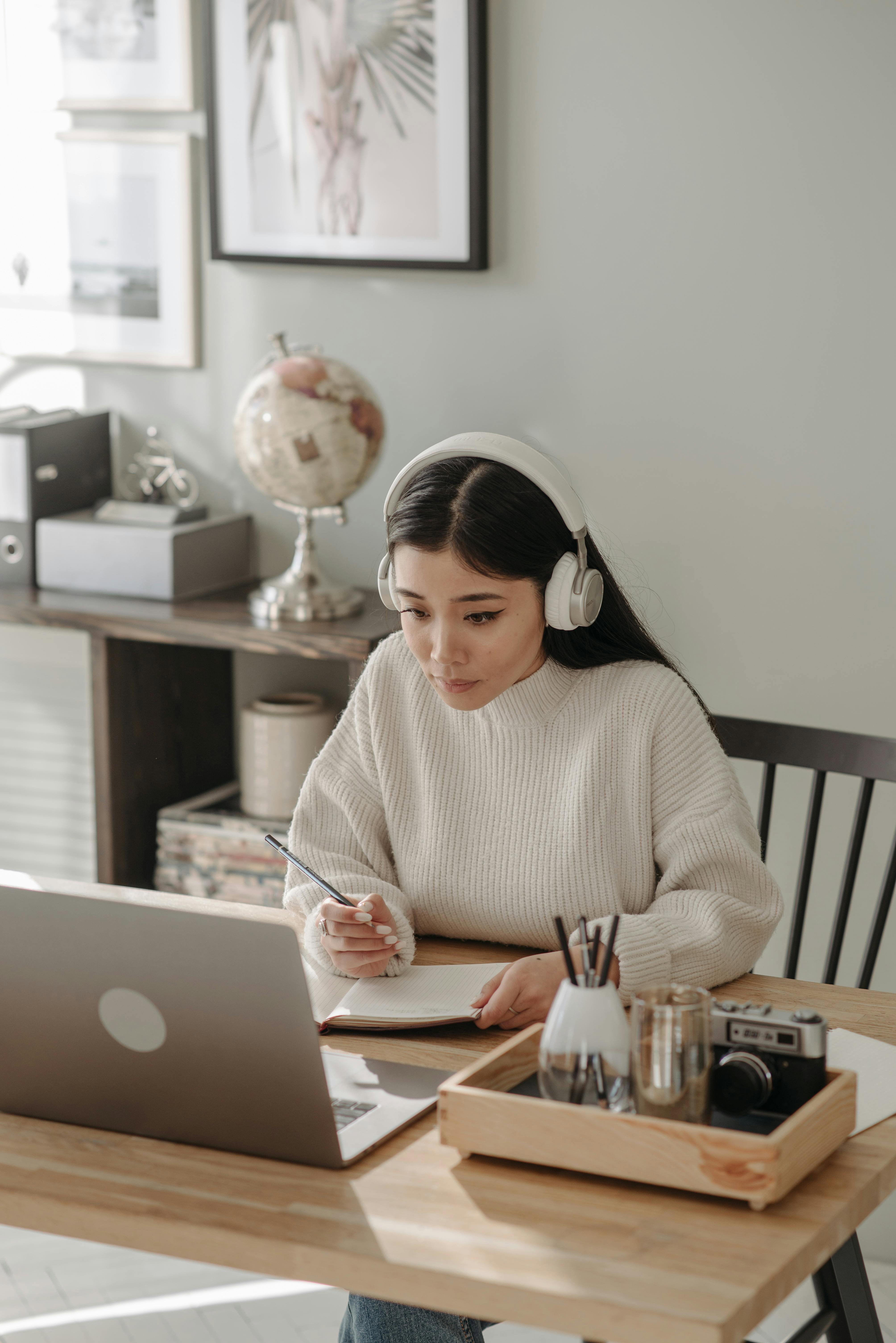 A cybersecurity professional taking notes from a laptop, wearing headphones. 