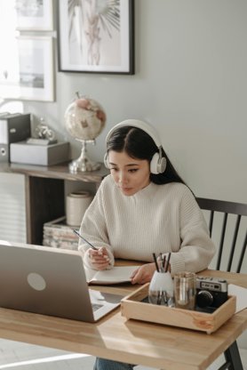 A cybersecurity professional taking notes from a laptop, wearing headphones.